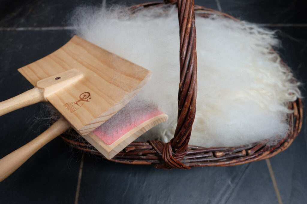 Basket of fluffy fleece with hand carders, ready for preparing and spinning into yarn.