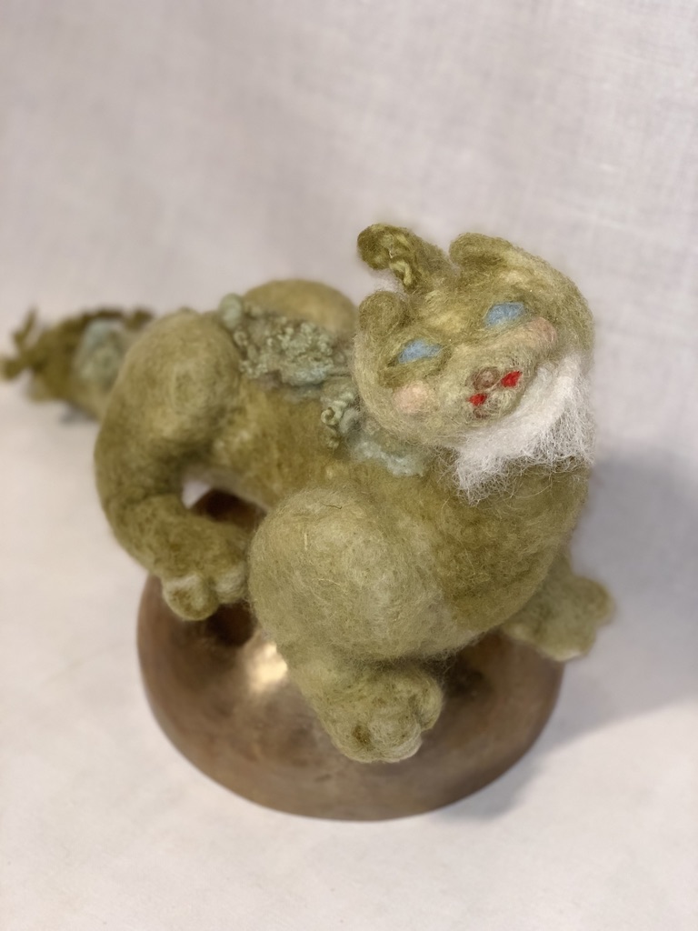 Needle-felted green dragon with blue eyes, white beard and curled back.